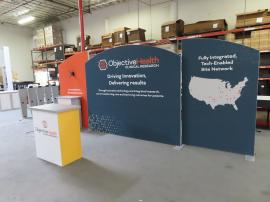 Customized 10 x 20 Symphony Portable Display with SEG Fabric Graphics, Monitor Mount, SYM-407B Backwall Counter with Locking Storage, and MOD-1703 Reception Counter with Backlit Graphics