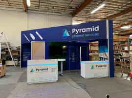 RENTAL: Island Design with L-Shaped Gravitee Panel System Backwall @ 12 ft. High, S44 Extrusion Framed Frosted Acrylic Sections, Elevated Angled Bridged Gravitee Header, (2) Large Monitor Mounts, (4) LED Arm Lights, Custom &ldquo;Living" Faux Ivy Panel, RE-15
